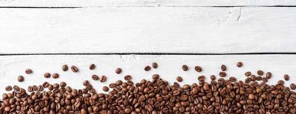 Roasted coffee beans on white wooden background with copyspace. Top view. Banner - 写真・画像