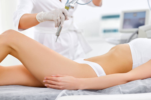 Crop unrecognizable cosmetologist performing laser procedure on legs of female client in modern beauty center - Fotoğraf, Görsel