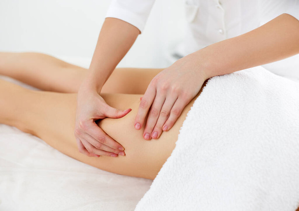 Zabiegi kosmetyczne dla utraty wagi. Przycięte ujęcie terapeuty lub masażysty robiącego drenaż limfatyczny lub masaż antycellulitowy na nogach dla klientki leżącej w centrum spa. Koncepcja pielęgnacji ciała - Zdjęcie, obraz