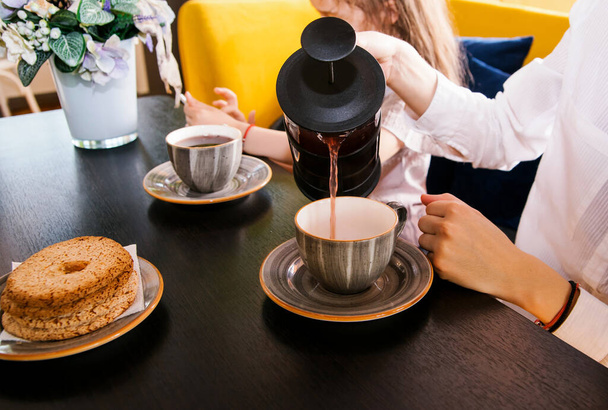 Women's hands pour tea from a teapot into beautiful cups. Tea party in a cafe. Morning family breakfast. Caring for your loved ones. - Photo, image