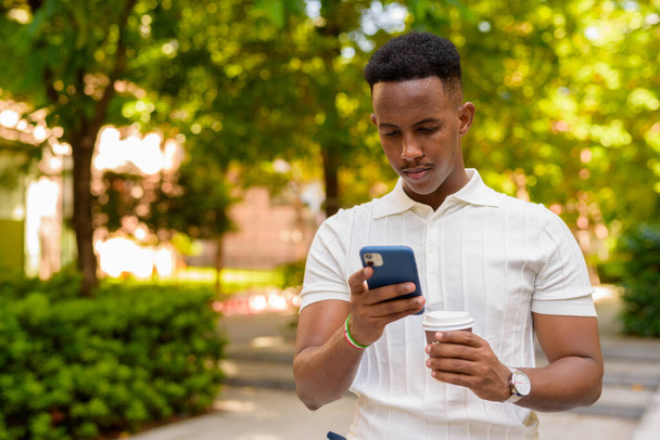 Porträt eines selbstbewussten jungen afrikanischen Geschäftsmannes, der lässig gekleidet ist und Mobiltelefone benutzt - Foto, Bild