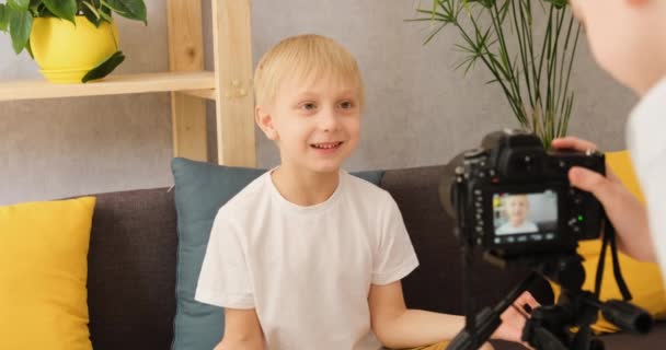 Twee jonge jongens maken content voor video blog op camera thuis op de bank. Creativiteit van kinderen op internet - Video