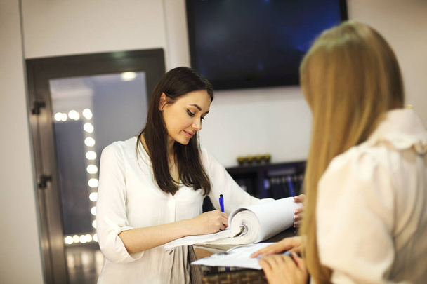 Young female receptionist working in beauty salon and writing down appointment of anonymous female customer - Photo, Image