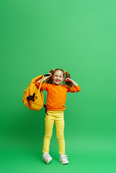 Back to school. happy little schoolgirl with two ponytails, in fashionable clothes and with backpack shows off her muscles. confident, strong and successful girl smiles and poses on green background. - Fotografie, Obrázek