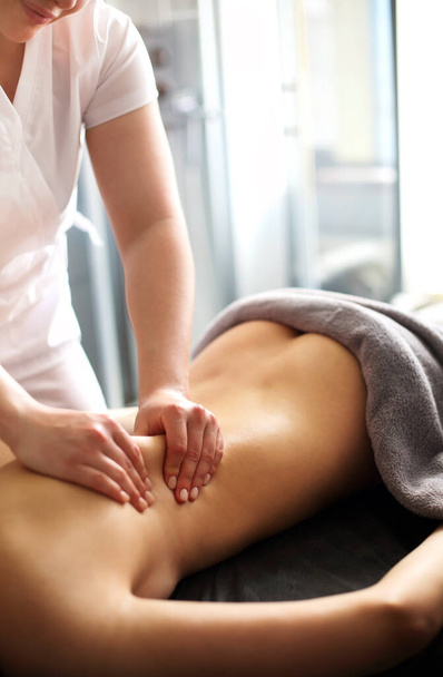 Maître sans visage donnant massage des muscles du dos et des épaules à une femme anonyme allongée sur la table dans un salon de spa - Photo, image