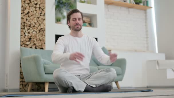 Rauhallinen nuori mies meditoi joogamatolla kotona - Materiaali, video