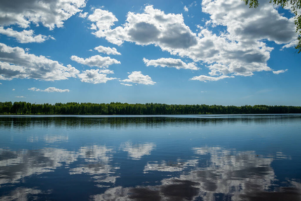 Beautiful summer nature landscape with a lake under a blue sky with white cumulus clouds reflecting in the clear water of the lake. - Photo, Image