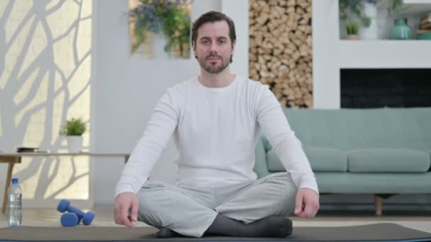 Porträt eines jungen Mannes, der zu Hause Yoga auf einer Yogamatte macht - Filmmaterial, Video