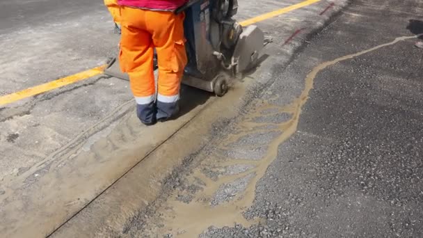 Pracownik używa tarczowej piły diamentowej do precyzyjnego cięcia asfaltu. Wykorzystuje działanie ścierne do przecięcia materiału, gdy piła obraca się z dużą prędkością. - Materiał filmowy, wideo