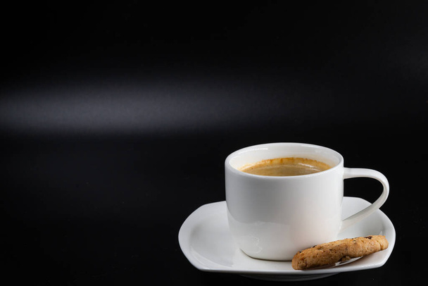 Weiße Kaffeetasse mit Keks und Kaffee auf schwarzem Hintergrund - Foto, Bild