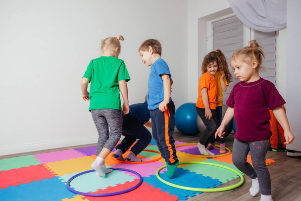 Children running and jumping around multicolor hoops on a floor - Foto, afbeelding