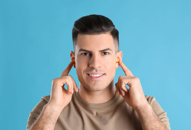 Man inserting foam ear plugs on light blue background - Foto, Imagem