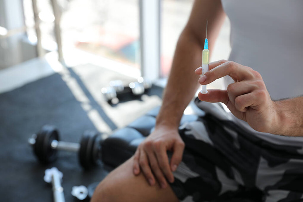 Sportsman with syringe in gym, closeup. Doping concept - Фото, изображение