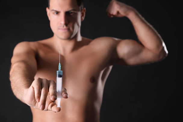 Athletic man with syringe against black background, focus on hand. Doping concept - Foto, immagini