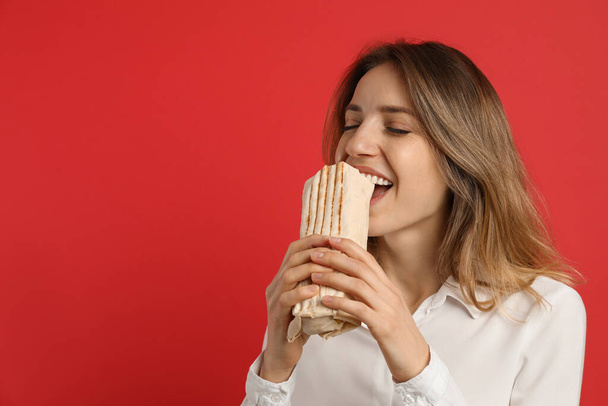 Young woman eating delicious shawarma on red background, space for text - Valokuva, kuva