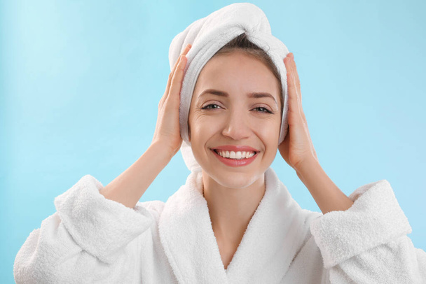 Beautiful young woman with hair wrapped in towel after washing on light blue background - Fotoğraf, Görsel