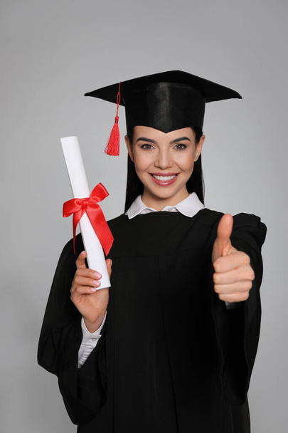 Happy student with graduation hat and diploma on grey background - Foto, imagen