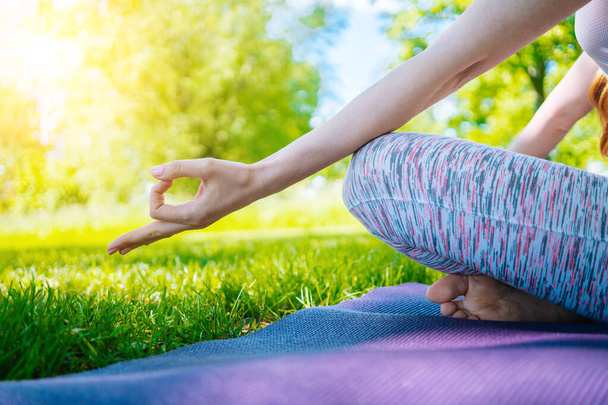 Młoda kobieta uprawiająca jogę w parku. Dziewczyna rozciąga ćwiczenia w pozycji do jogi. szczęśliwa i zdrowa kobieta siedząca w pozycji lotosu i ćwicząca jogę. medytacja i sport na zachodzie słońca na zewnątrz. - Zdjęcie, obraz