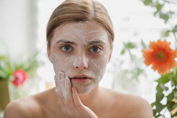 Beautiful young girl cleansing face with cosmetic facial skincare foam, gel or soap. Woman hame SPA procedures. - Photo, image