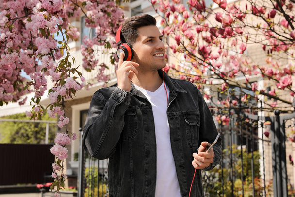 Happy man with smartphone listening to audiobook outdoors on spring day - Фото, изображение