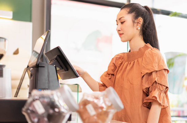 Left side of beautiful Asian woman customer choosing kind of coffee on cashier screen in front of coffee bar. Barista work at coffee bar and food service business - Valokuva, kuva