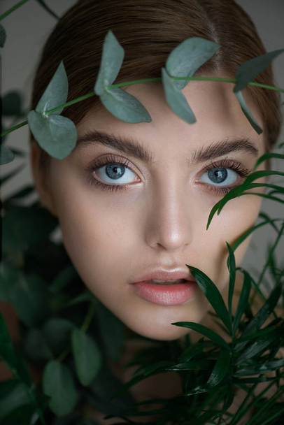 Portrait of beauty model with natural nude makeup with eucalyptus leaf branch and tropical plants.  Beautiful young woman with clean perfect skin in greens. Spa, skincare and wellness. Close up. - Zdjęcie, obraz