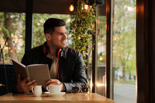 Man with headphones and book at table in cafe - Foto, Imagen