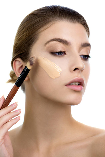 Young woman applying facial foundation cream at her face. Beauty model with perfect fresh skin and long eyelashes cares about her skin at home. Makeup Concept. - Φωτογραφία, εικόνα