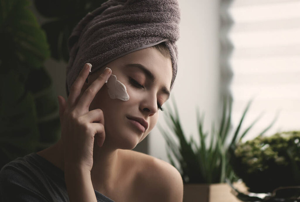 Young woman applying face cream on her face. Beauty model with perfect fresh skin cares about her skin at home. Spa and Wellness, Skin Care Concept. Close up, selected focus. - Fotografie, Obrázek