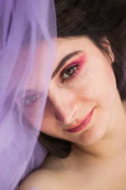 Обличчя дівчини з закритою тканиною для очей і макіяжем рожевим і блискітками на фіолетовому фоні
 - Фото, зображення