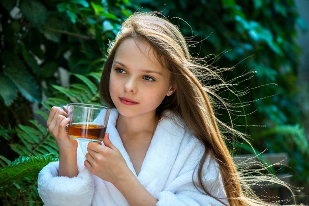 Cute little girl is drinking tea on green backgraund.  Kid holds hot beverage. - Foto, Imagem