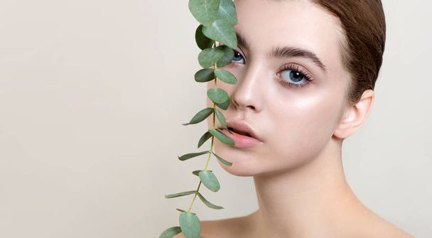 Portrait of beauty model with natural nude makeup with eucalyptus leaf branch.  Beautiful young woman with clean perfect skin on light backgroung. Spa, skincare and wellness. Close up. - Foto, Imagen