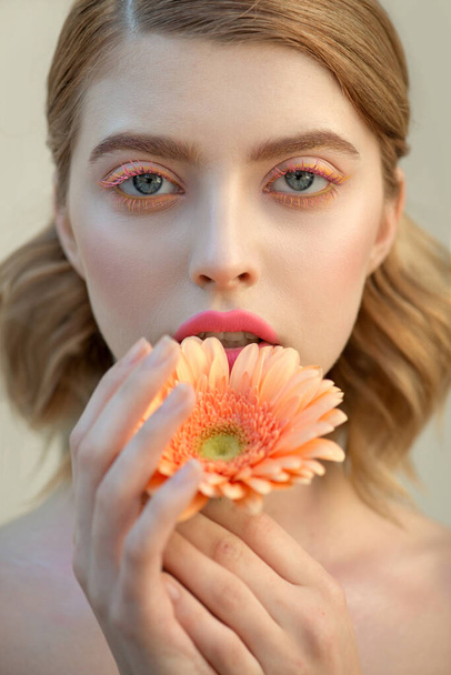 Fashion model with creative professional make-up with pink and yellow color mascara and gerbera flower in hand. SPA, wellness, bodycare and skincare concept. - Fotoğraf, Görsel