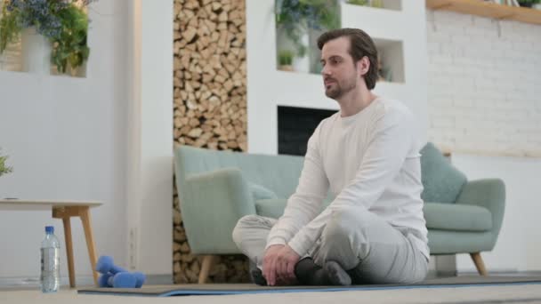Młody człowiek medytujący na matę do jogi w domu - Materiał filmowy, wideo