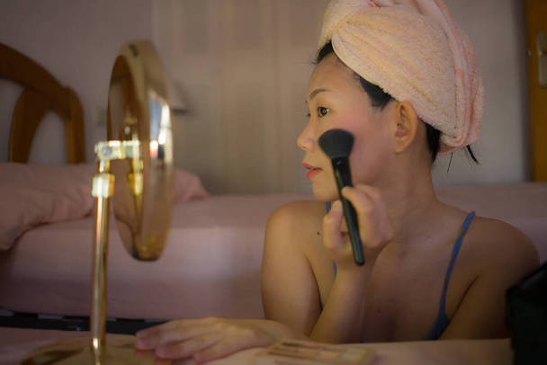 lifestyle portrait of young beautiful and happy Asian woman applying makeup and beauty facial treatment looking in mirror at home bedroom cheerful before dating - Zdjęcie, obraz