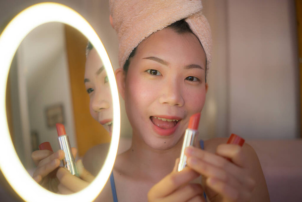 lifestyle portrait of young beautiful and happy Asian woman applying makeup and beauty facial treatment looking in mirror at home bedroom cheerful before dating - Photo, Image