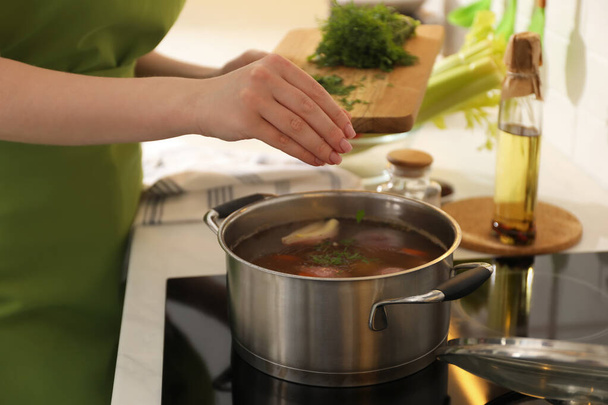Woman putting dill into pot to make bouillon in kitchen, closeup. Homemade recipe - Fotografie, Obrázek