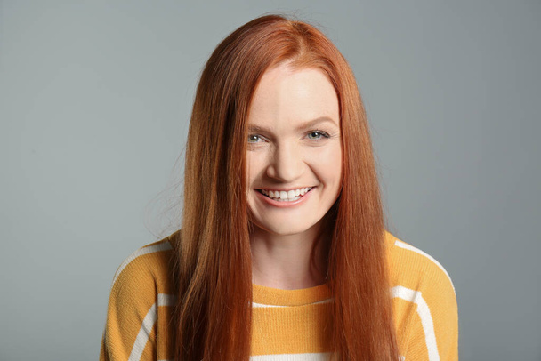 Candid portrait of happy young woman with charming smile and gorgeous red hair on grey background - 写真・画像