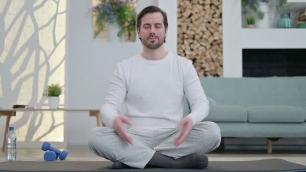 Porträt eines jungen Mannes, der zu Hause auf einer Yogamatte meditiert - Filmmaterial, Video
