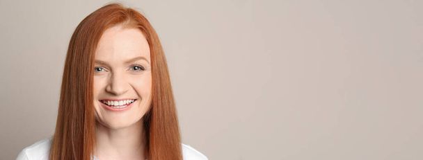 Candid portrait of happy young woman with charming smile and gorgeous red hair on beige background - 写真・画像