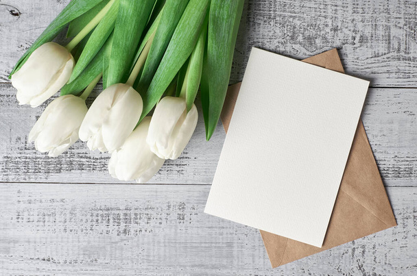 Greeting card mockup with envelope and tulip flowers bouquet on wooden background, top view, copy space - Foto, immagini