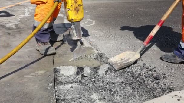 Robotnik budowlany łamie asfalt pneumatycznym młotem pneumatycznym. Człowiek za pomocą łopaty podnieść i wyrzucić popękane części. - Materiał filmowy, wideo