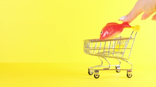 Shopping cart with fish inside on a yellow background, closeup. Black Friday Shopping and Discount Concept. - Footage, Video