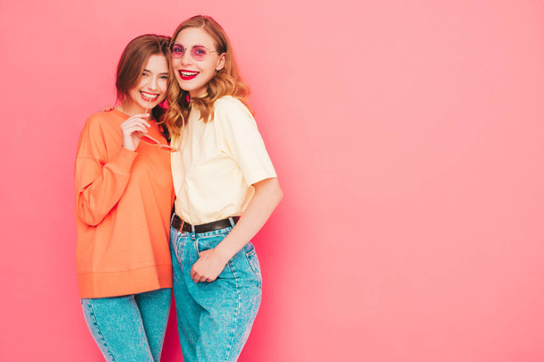 Two young beautiful smiling hipster female in trendy summer hipster  clothes. Sexy carefree women posing near pink wall in studio. Trendy and positive models having fun. Cheerful and happy - Fotó, kép