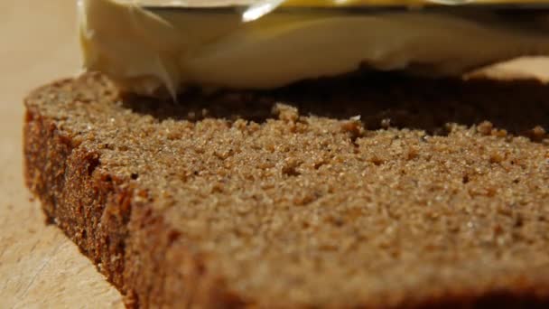 Rozsiewanie masła wegańskiego na chlebie żytnim bez nabiału i jaj. Nóż rozmazujący miękkie masło na kromce chleba o wschodzie słońca. Zbliżenie - Materiał filmowy, wideo