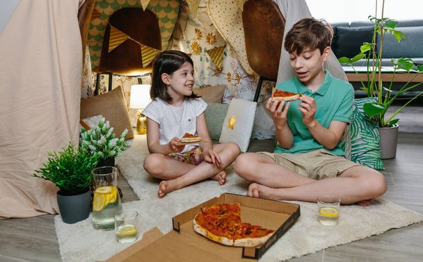Lapset syövät pizzaa ja limonadia leiriytyessään kotona - Valokuva, kuva