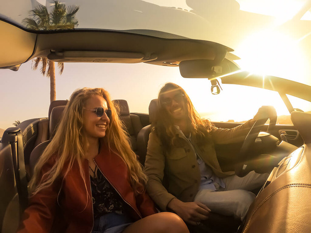Romantic couple enjoying holidays driving a convertible car on the road at sunset. People rent car at vacations. Transport , people and lifestyle. - Foto, Imagen