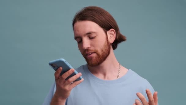 Çekici bir adam mavi arkaplanda izole bir şekilde duran bir sesli mesaj kaydediyor. - Video, Çekim