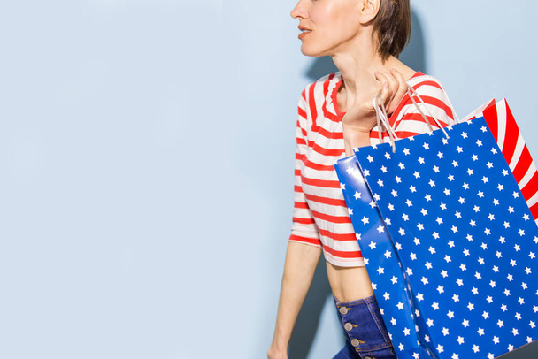 Happy shopping woman with shopping bags over blue background wearing striped clothing and shoping bags in patriotic colors - Φωτογραφία, εικόνα