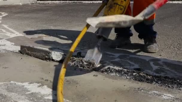 İnşaat işçisi pnömatik bir matkapla asfaltı kırıyor. Kırık parçaları toplayıp atmak için kürek kullanan bir adam.. - Video, Çekim